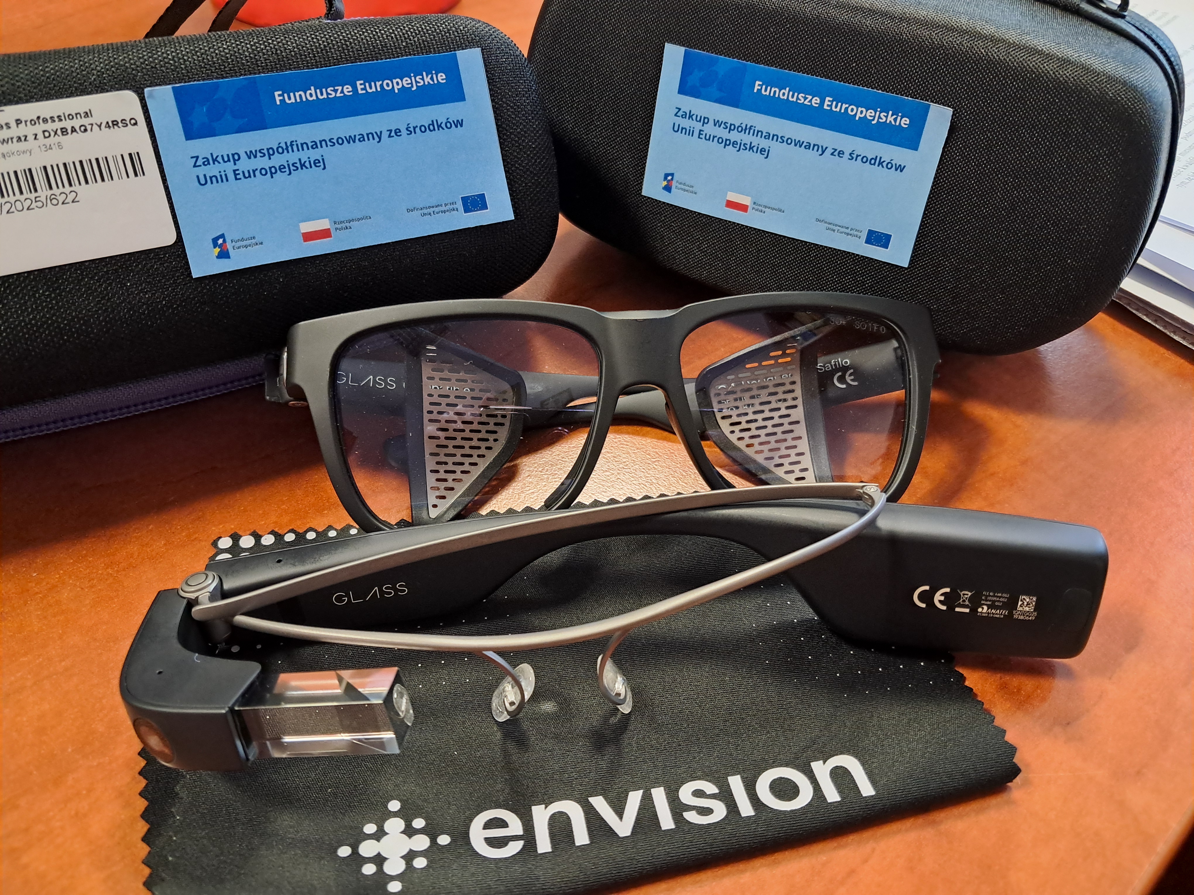 Okulary elektroniczne Envision wraz z etui i akcesoriami, ułożone na biurku
