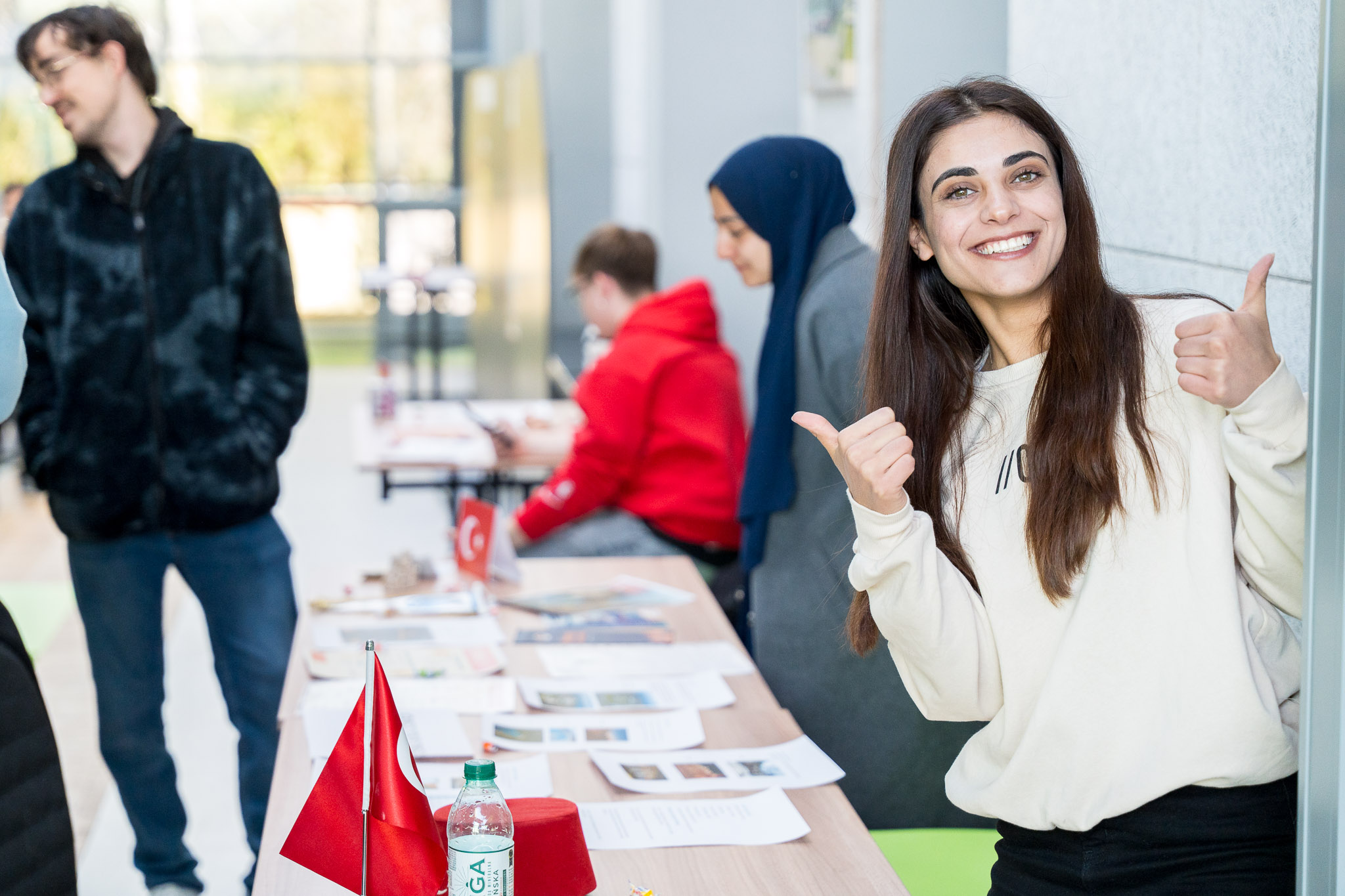 Studentka pokazuje kciuki do góry, w tle widać stół z ulotkami i flagą Turcji