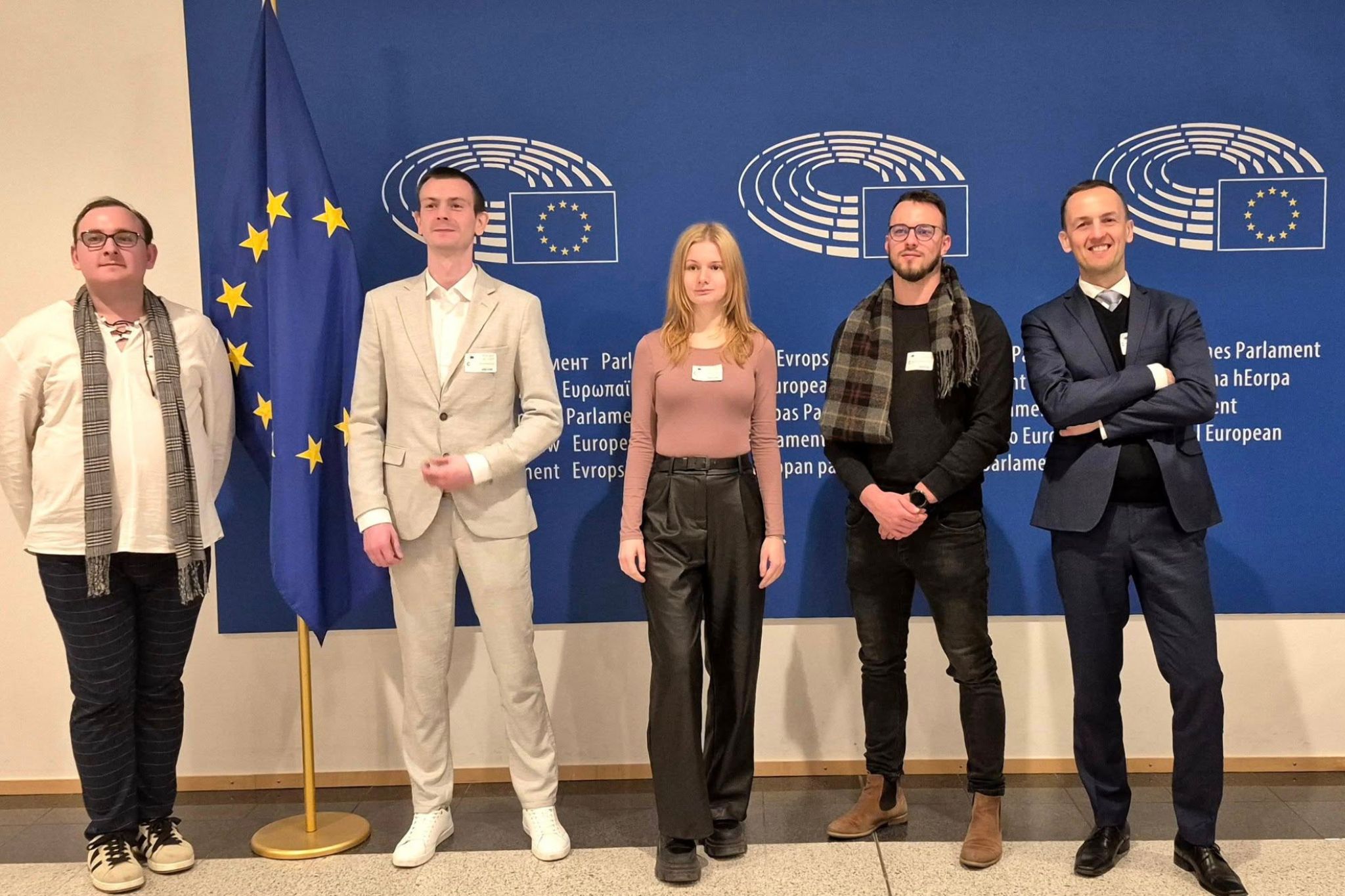 Pięć osób pozuje do zdjęcia na tle loga parlamentu europejskiego. 