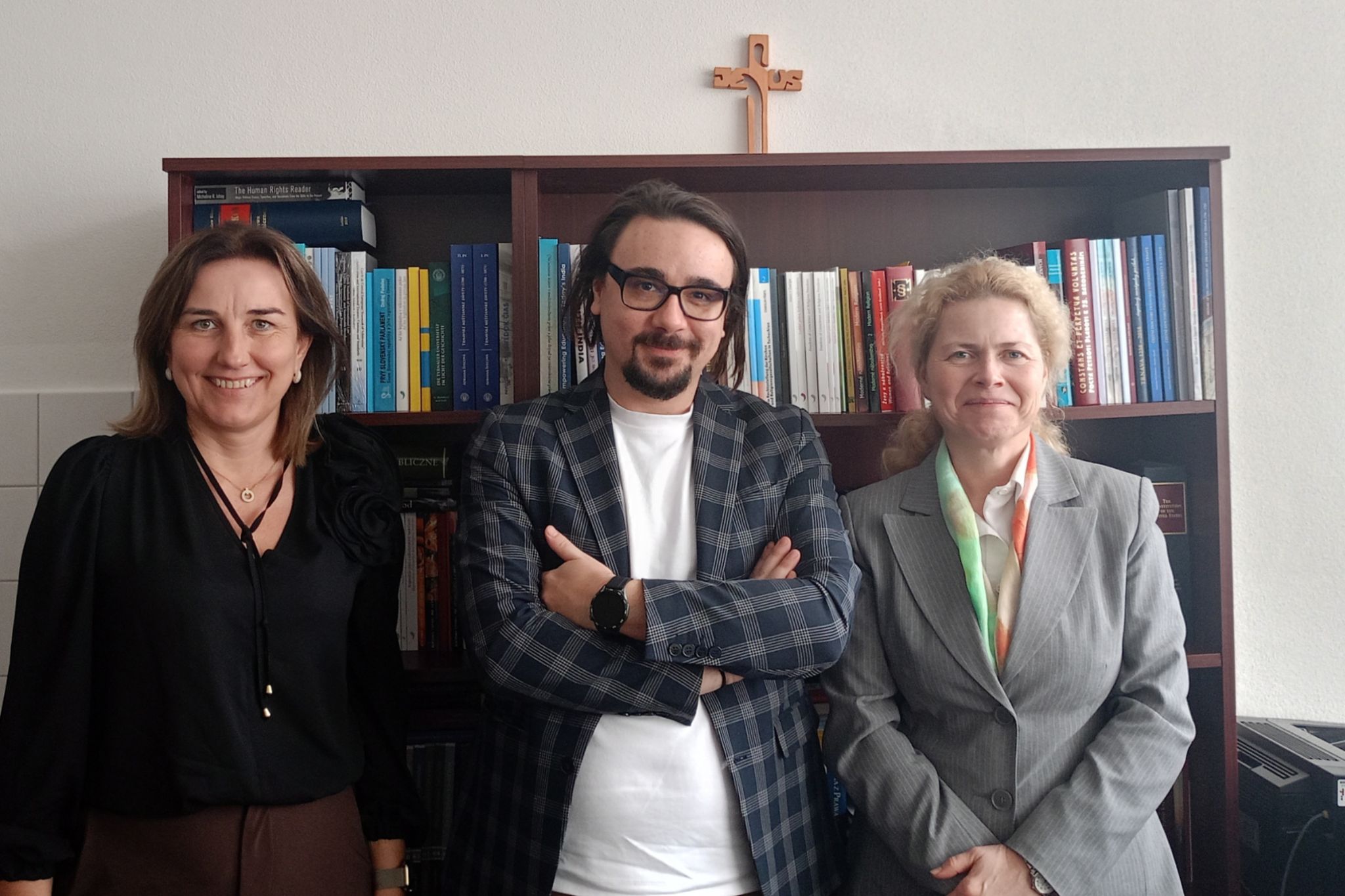 Trzy osoby pozują do zdjęcia na tle regału. Po środku mężczyzna, po bokach dwie Panie.