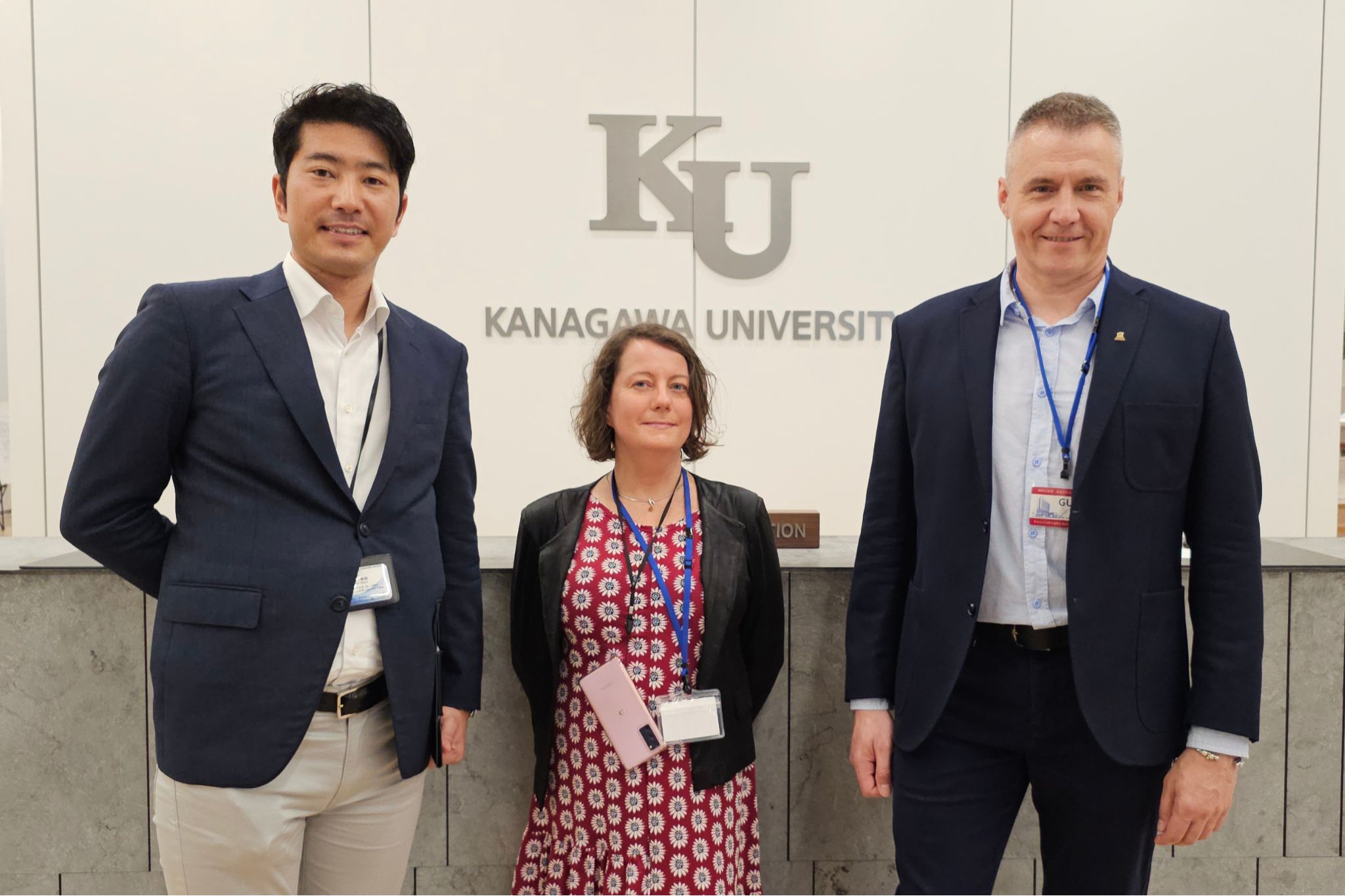 Trzy osoby na tle napisu z nazwą uczelni Kanagawa Unversity