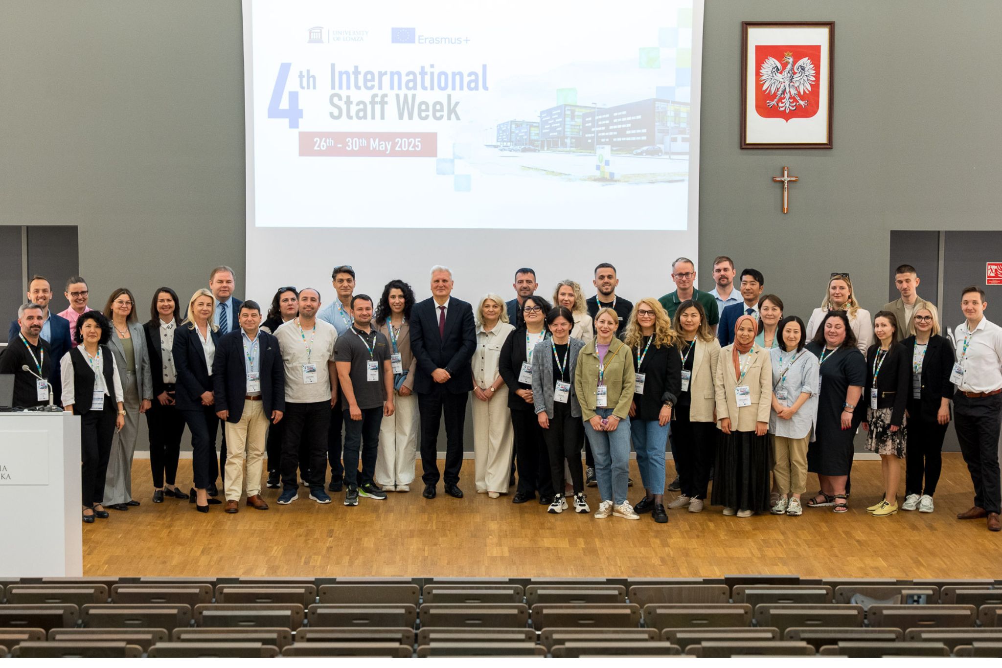 Grupa osó pozuje do zdjęcia na scenie, w tle wyświetla się napis IV International Staff Week