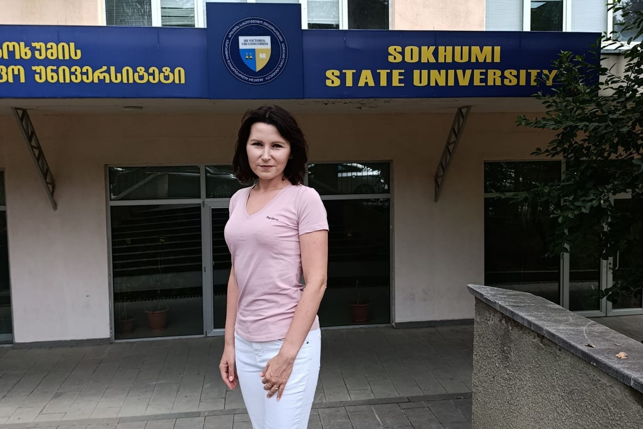 Kobieta w różowej koszulce na tle budynku Uczelni