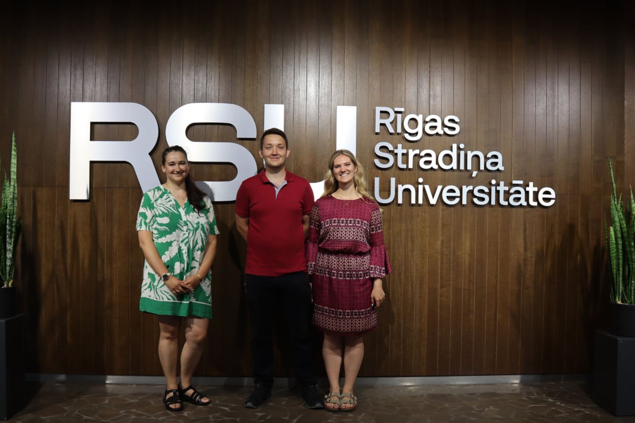 Trzy osoby na tle logo uczelni RSU, w środku budynku