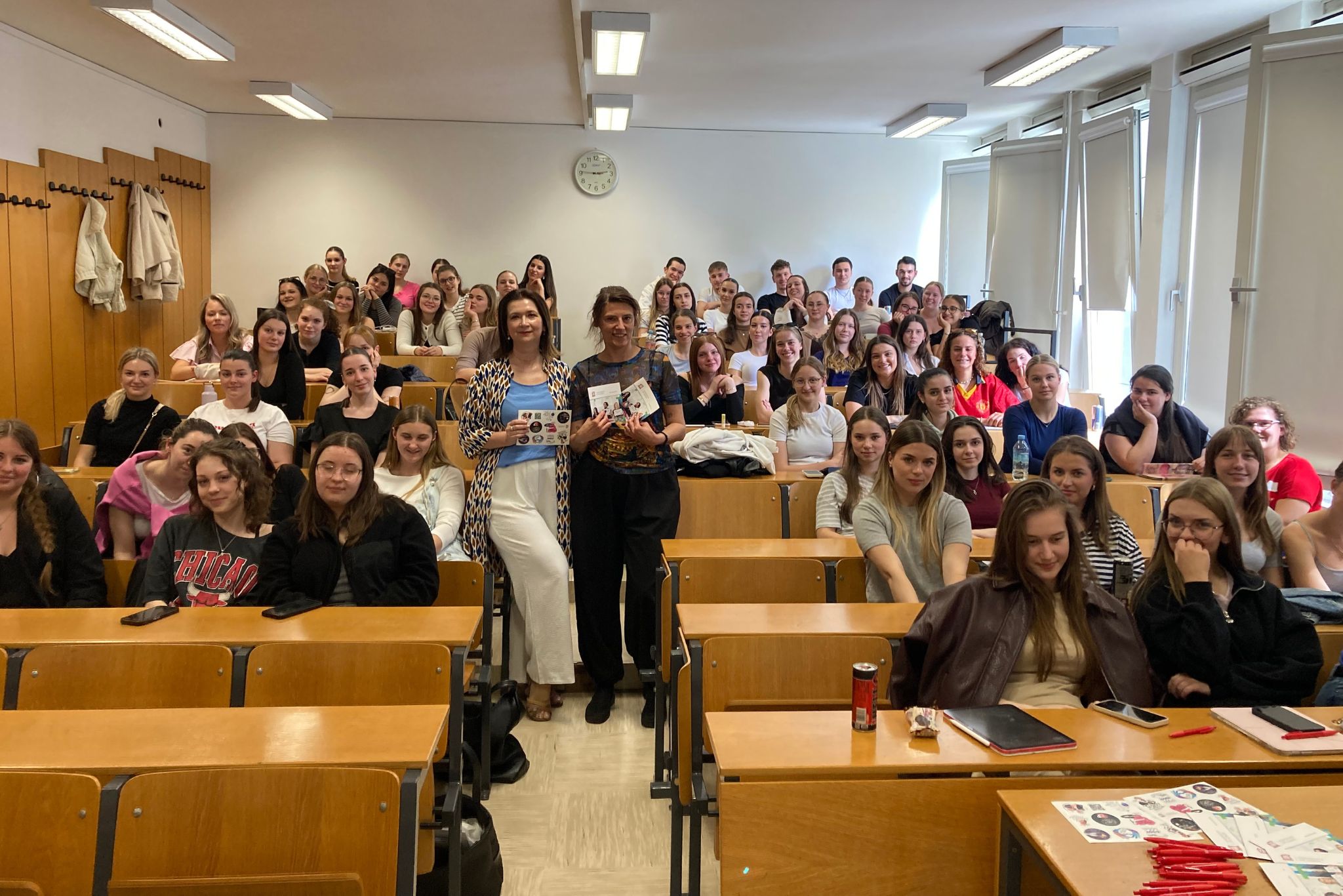 Dwie lektorki stoją na środku sali dookoło duża grupa studentów