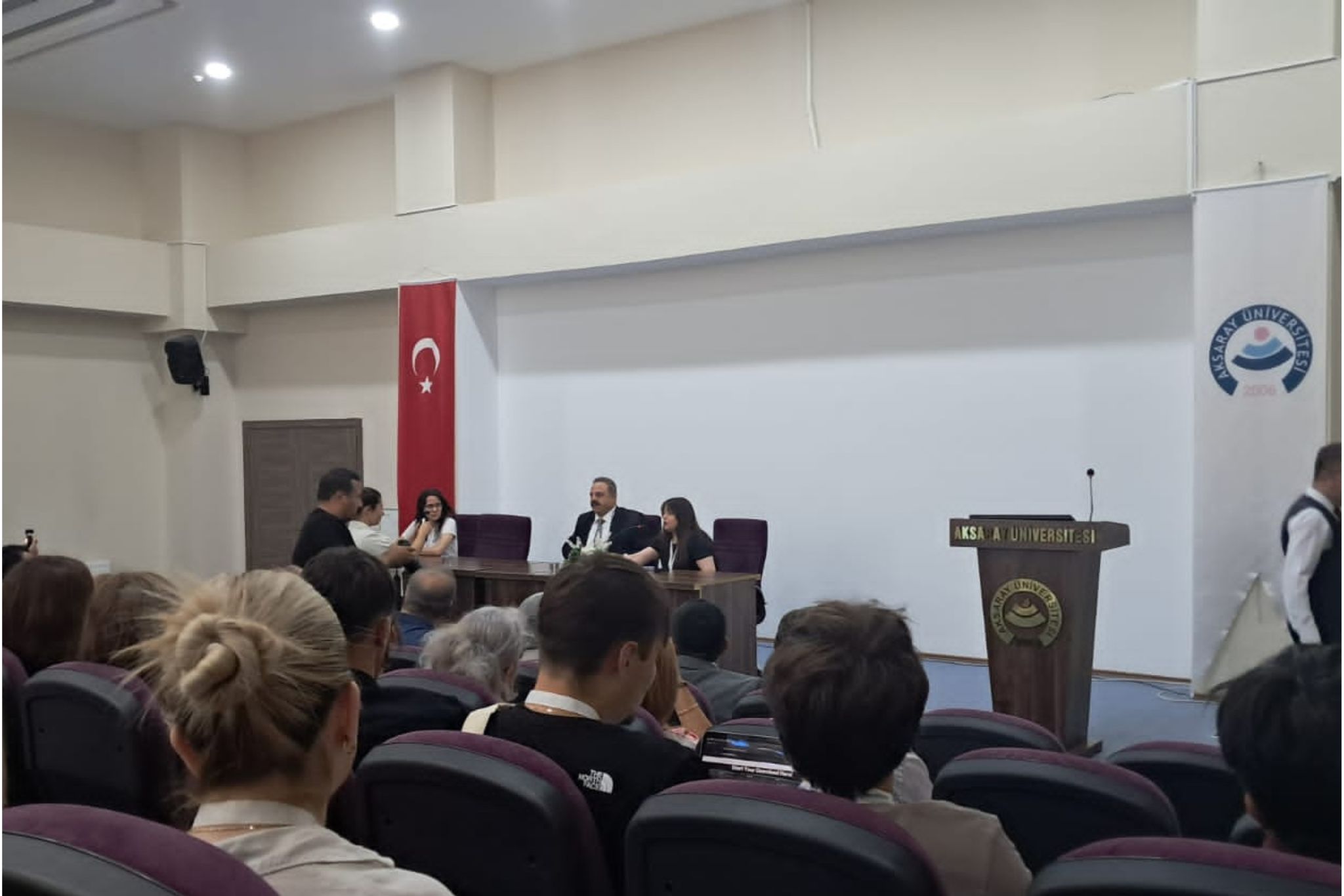 Aula, na dole widać mównicę i kilku mężczyzn w garniturach