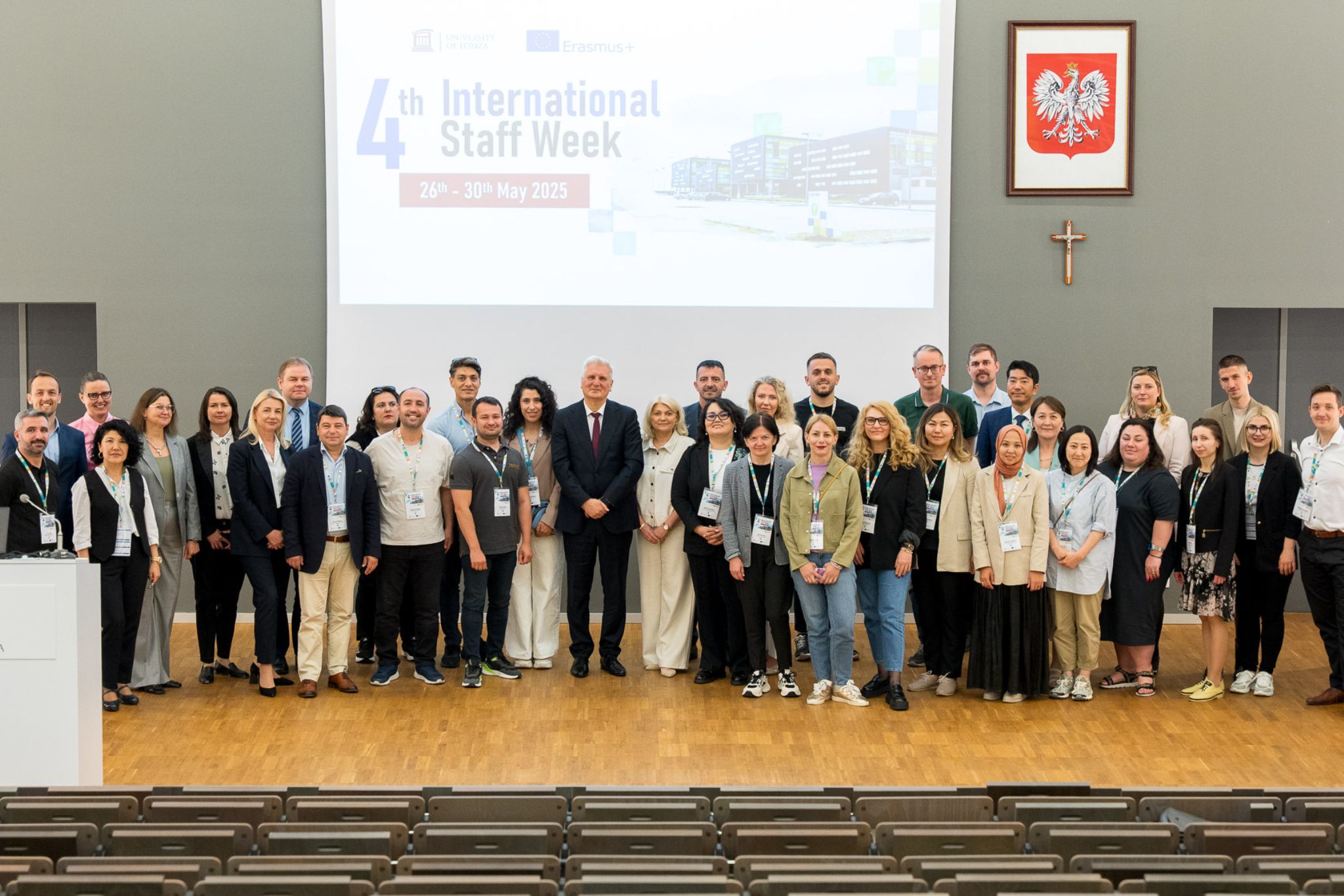 Zdjęcie grupowe uczestników wydarzenia, na ścianie w tle widoczny wyświetlony napis 4th International Staff Week