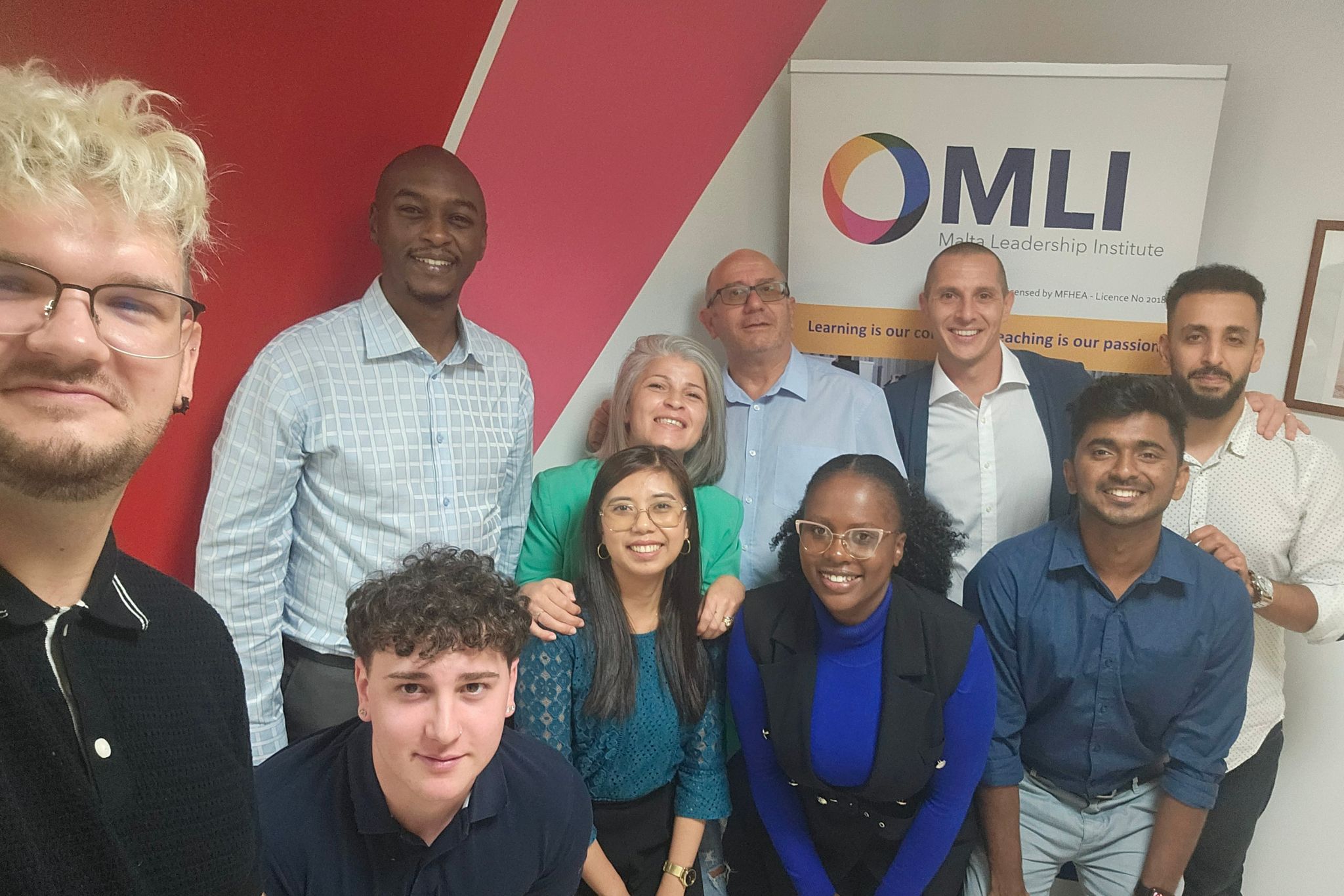 Grupa osób pozuje do zdjęcia na uczelni i banerem z jej logo