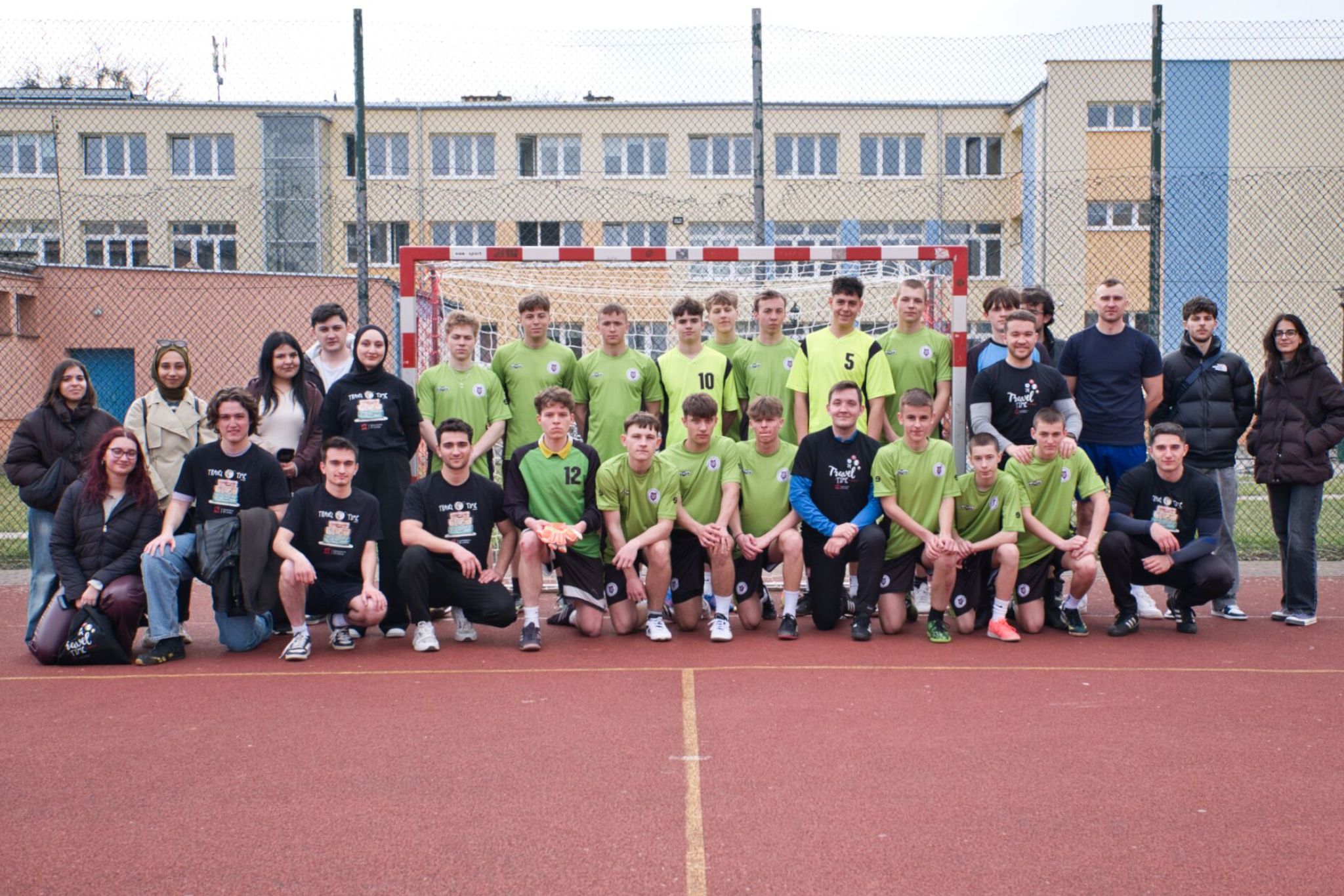 Grupa ludzi w sportowych ciuchach pozuje do zdjęcia na boisku 