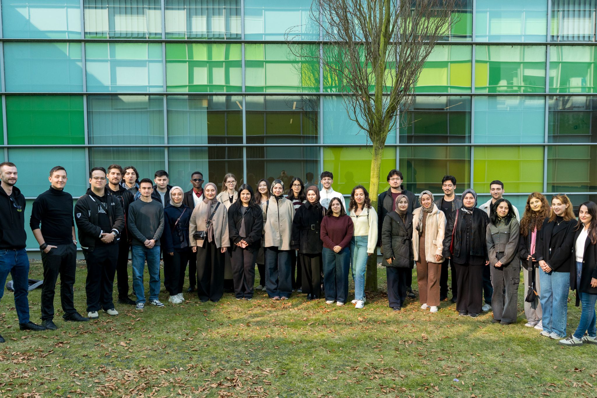 Grupa osób pozuje do zdjęcia na tle przeszkolonego budynku