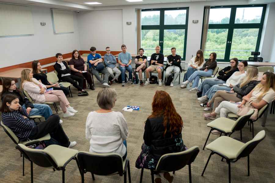 grupa studentów siedzi na krzesłach w okręgu w sali zajęciowej