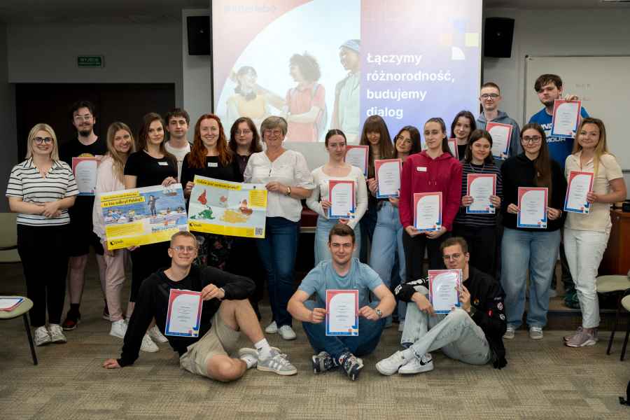 grupa studentów pozuje z certyfikatami w sali zajęciowej, za nimi ekran rzutnika
