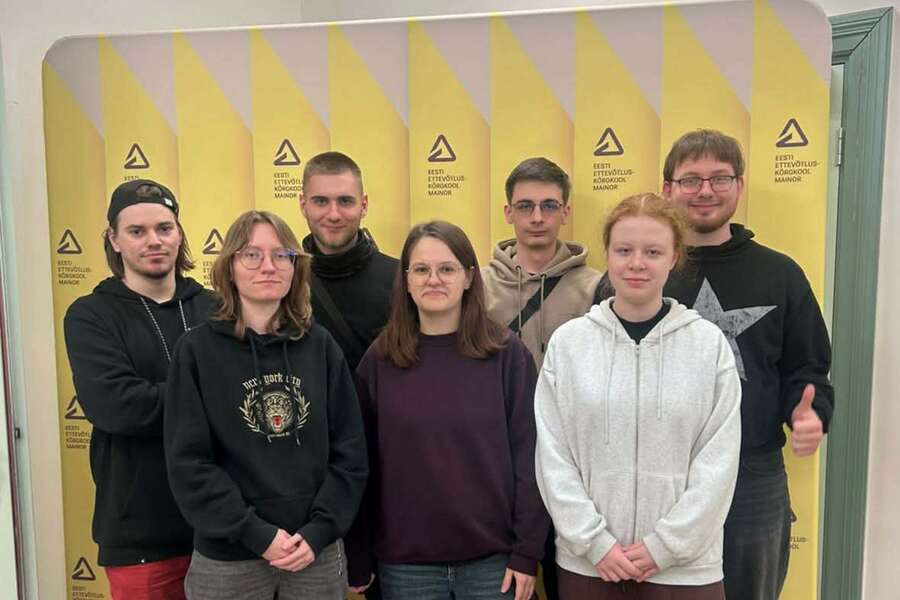 A group of seven people posing for a photo in front of a backdrop featuring the university’s logo.