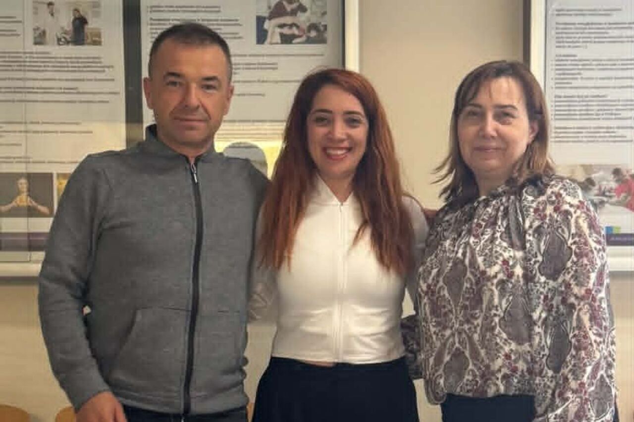 Three people are posing for a photo. Two women are on the right and in the center, and a man is on the left.