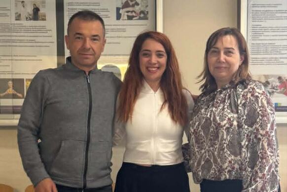 Three people are posing for a photo. Two women are on the right and in the center, and a man is on the left.