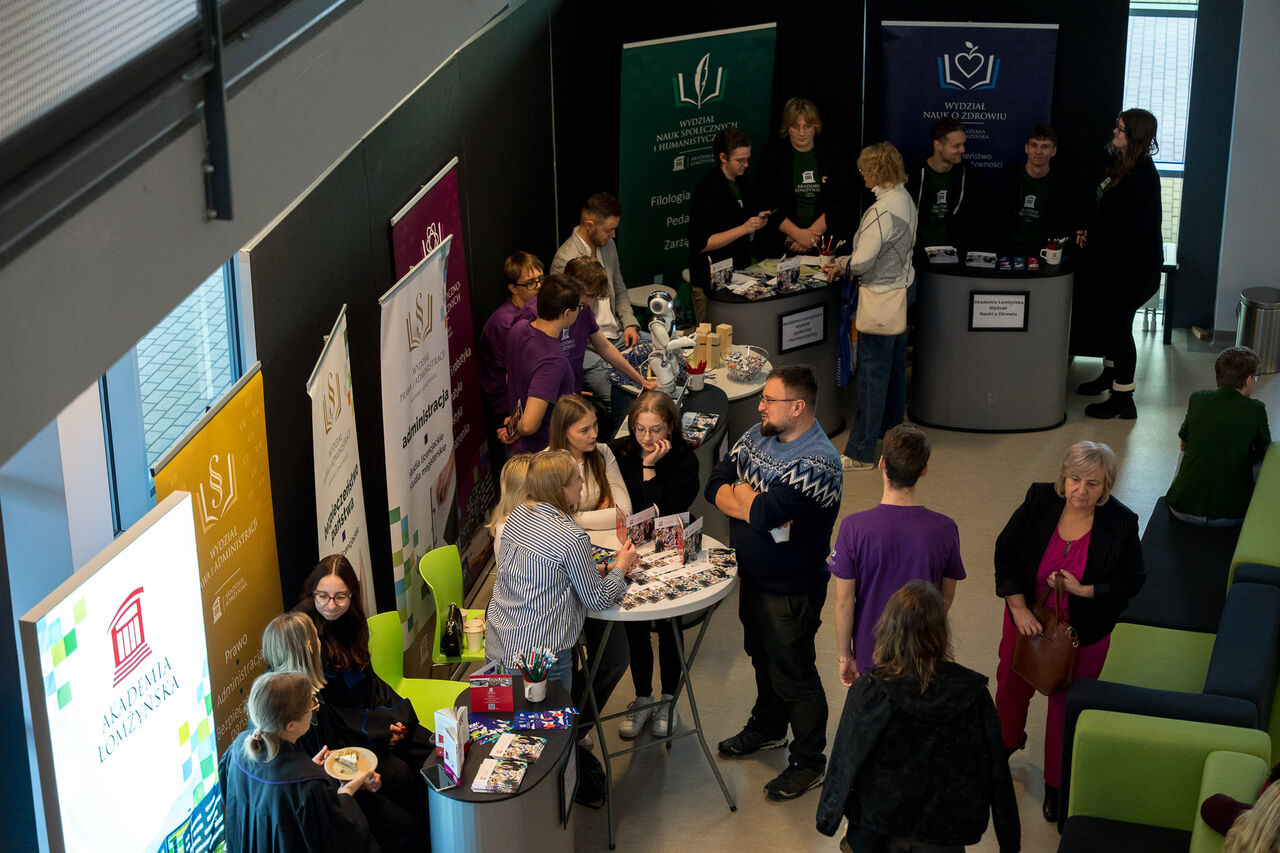 Information stands with promotional materials and leaflets during an event in the main hall, with several people talking at stands featuring university banners.