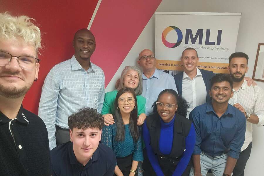 Grupa osób pozuje do zdjęcia na uczelni i banerem z jej logo