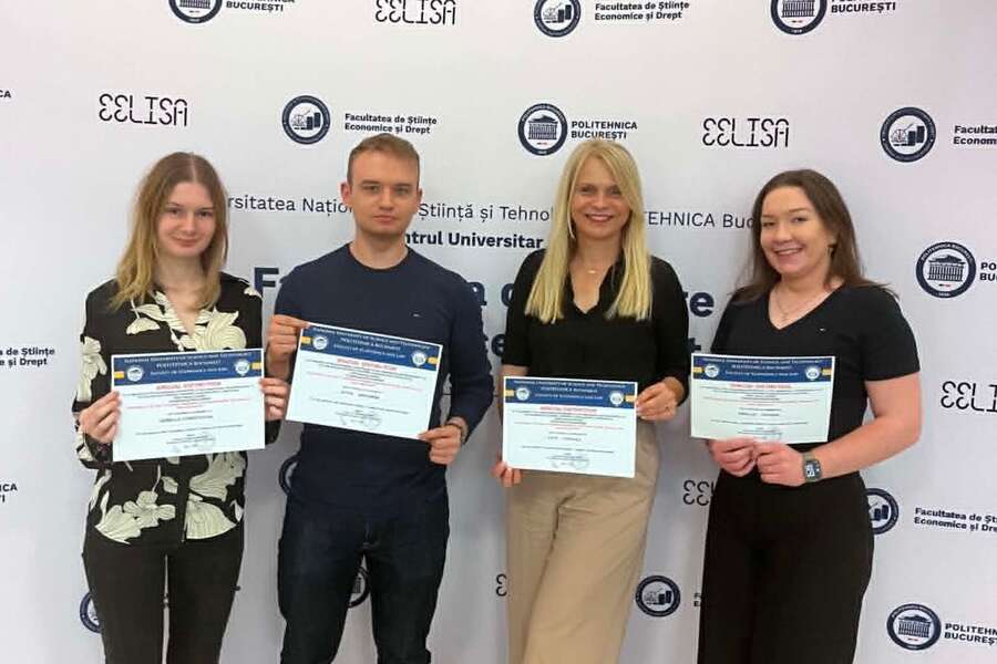 Four people holding certificates pose in front of a backdrop featuring the university’s logo and name.