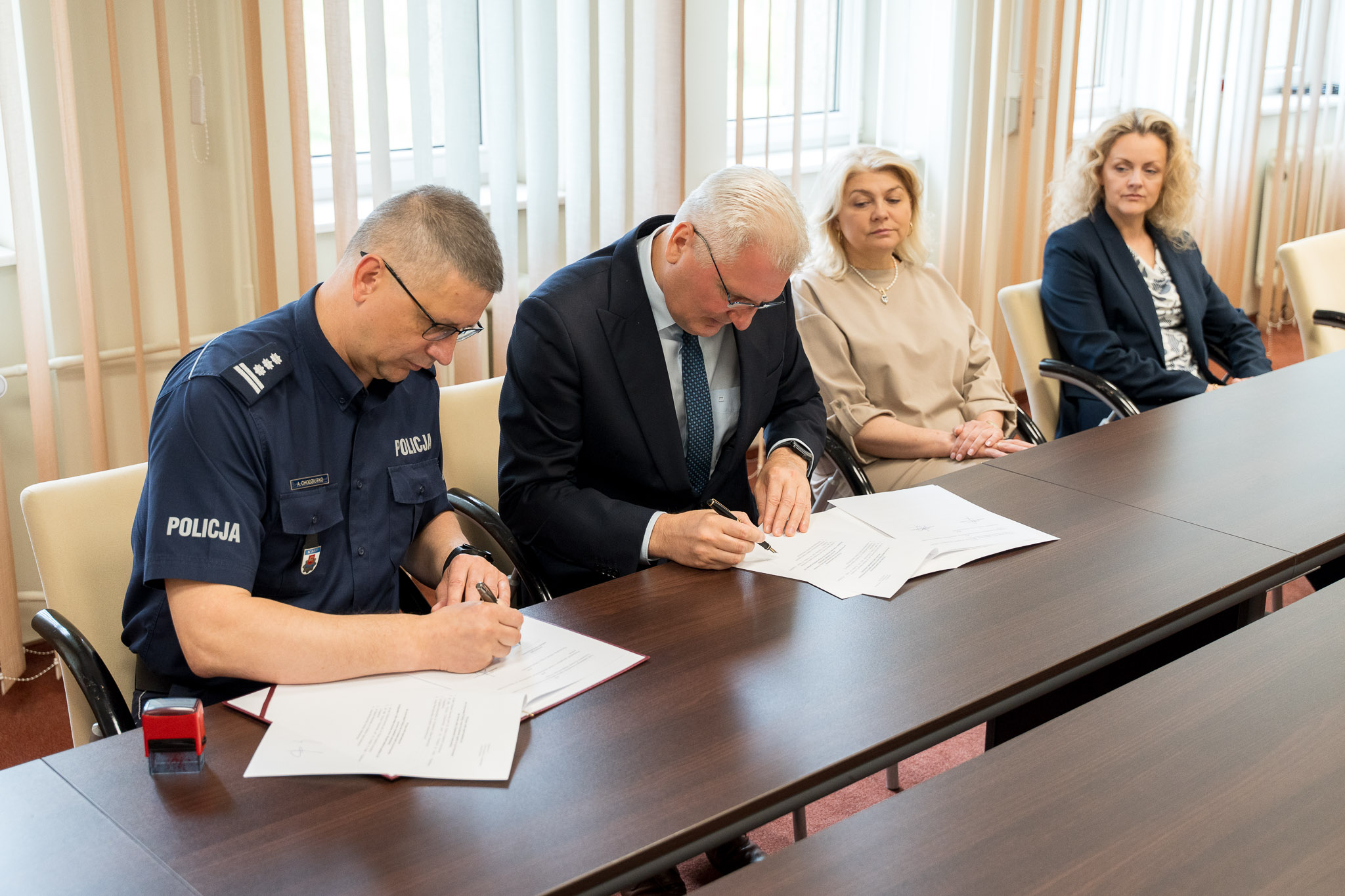 dwie osoby podpisują porozumienie, w tle dwie kobiety