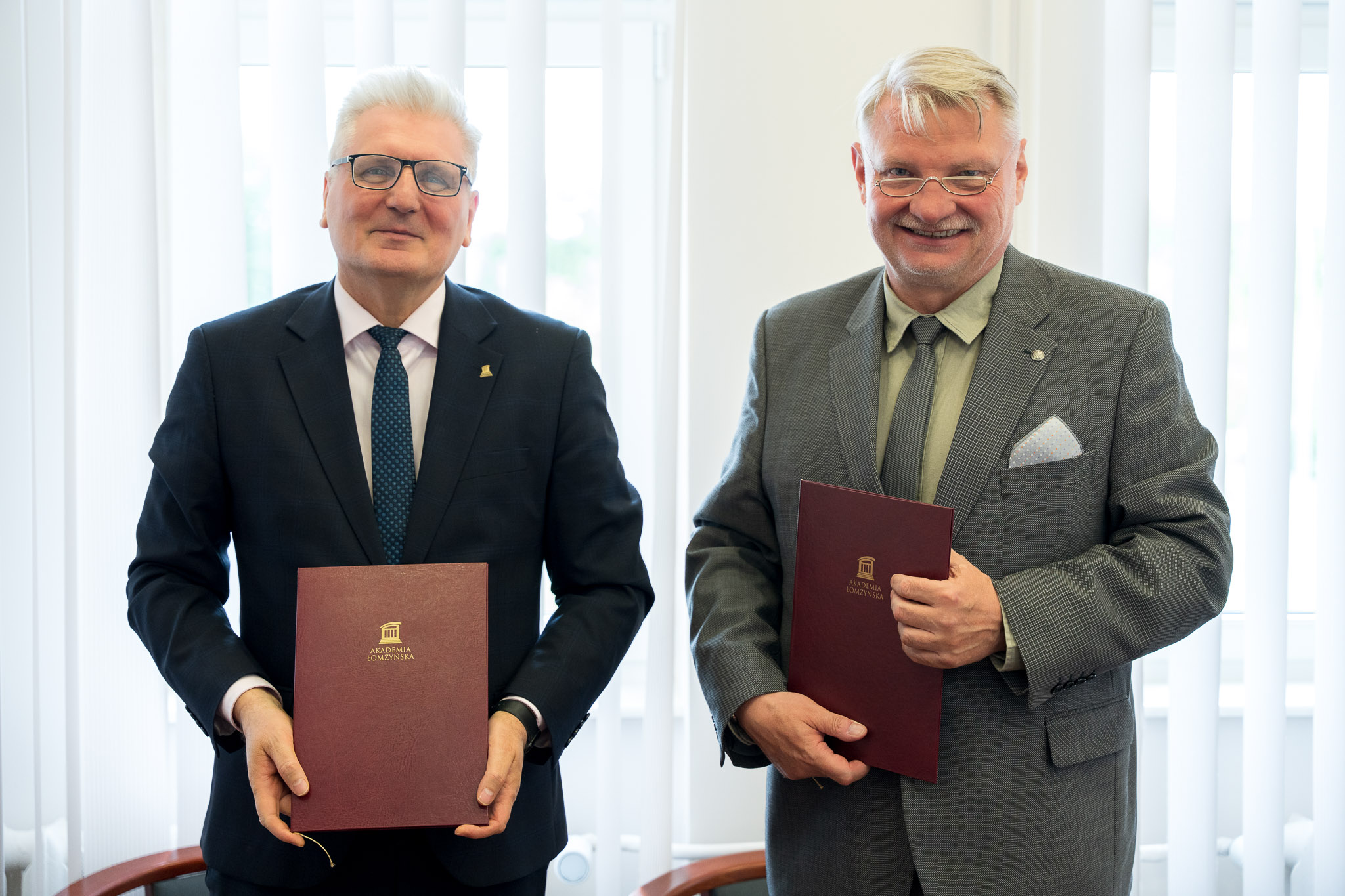 dwie osoby pozują do zdjęcia, w dłoniach trzymają teczki ał