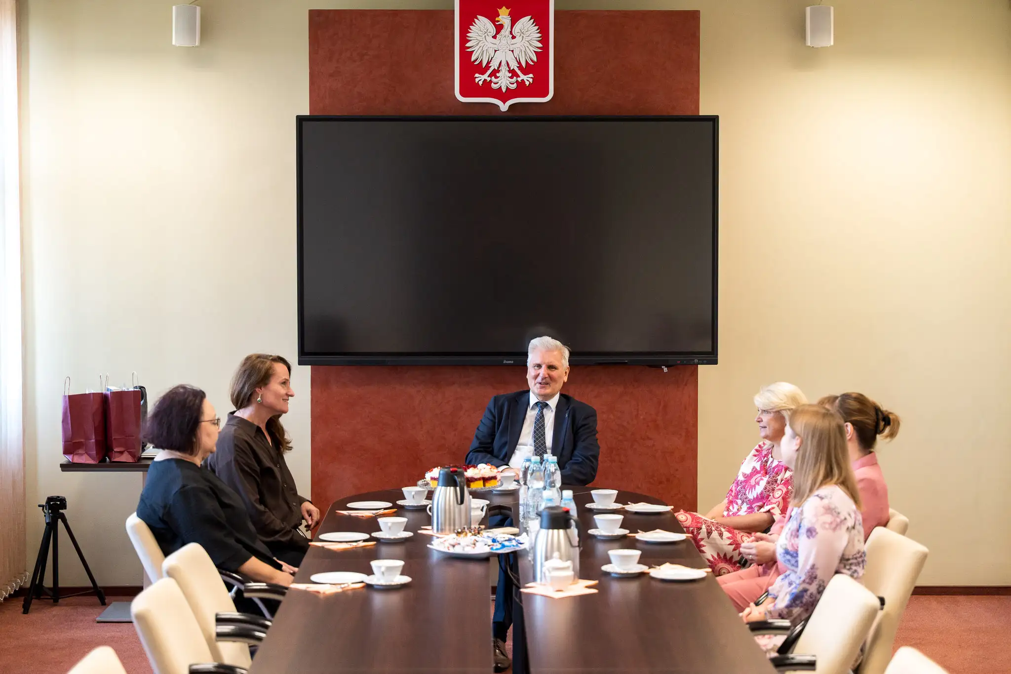 osoby przy stole prowadzą dyskusje, w tle godło Polski 