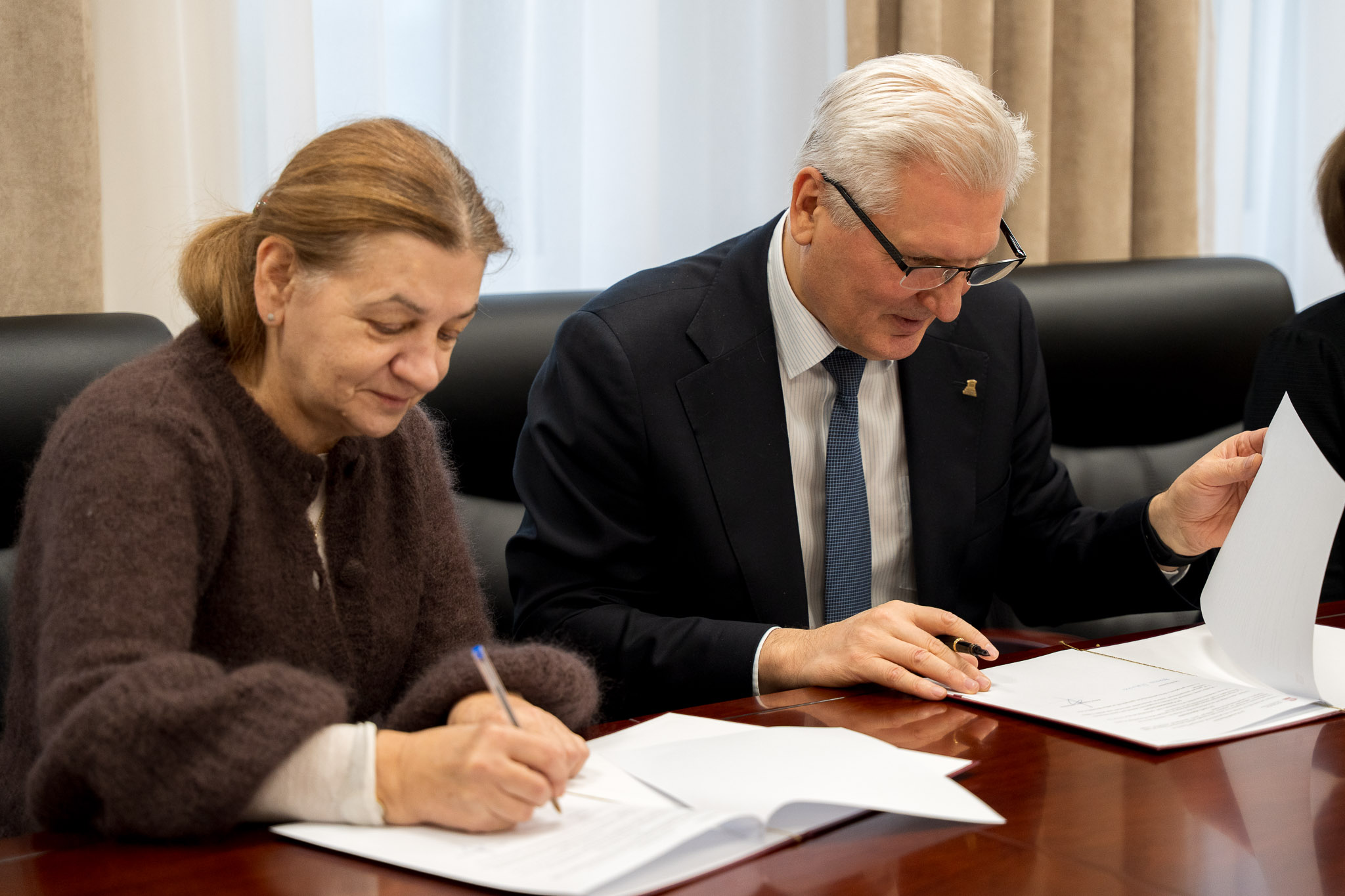 Dwie osoby stoją przy stole konferencyjnym, trzymają teczki i podają sobie ręce.