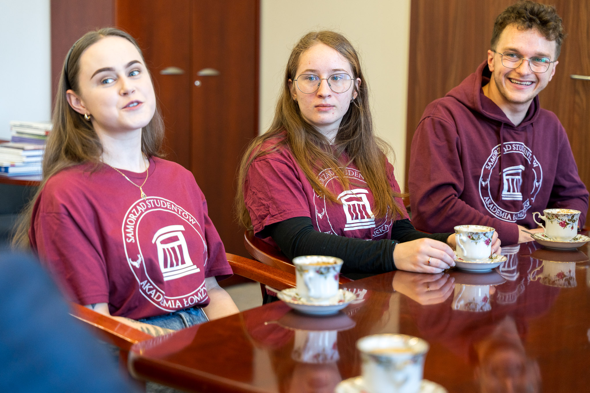 trzy osoby siedzą przy stole i rozmawiają