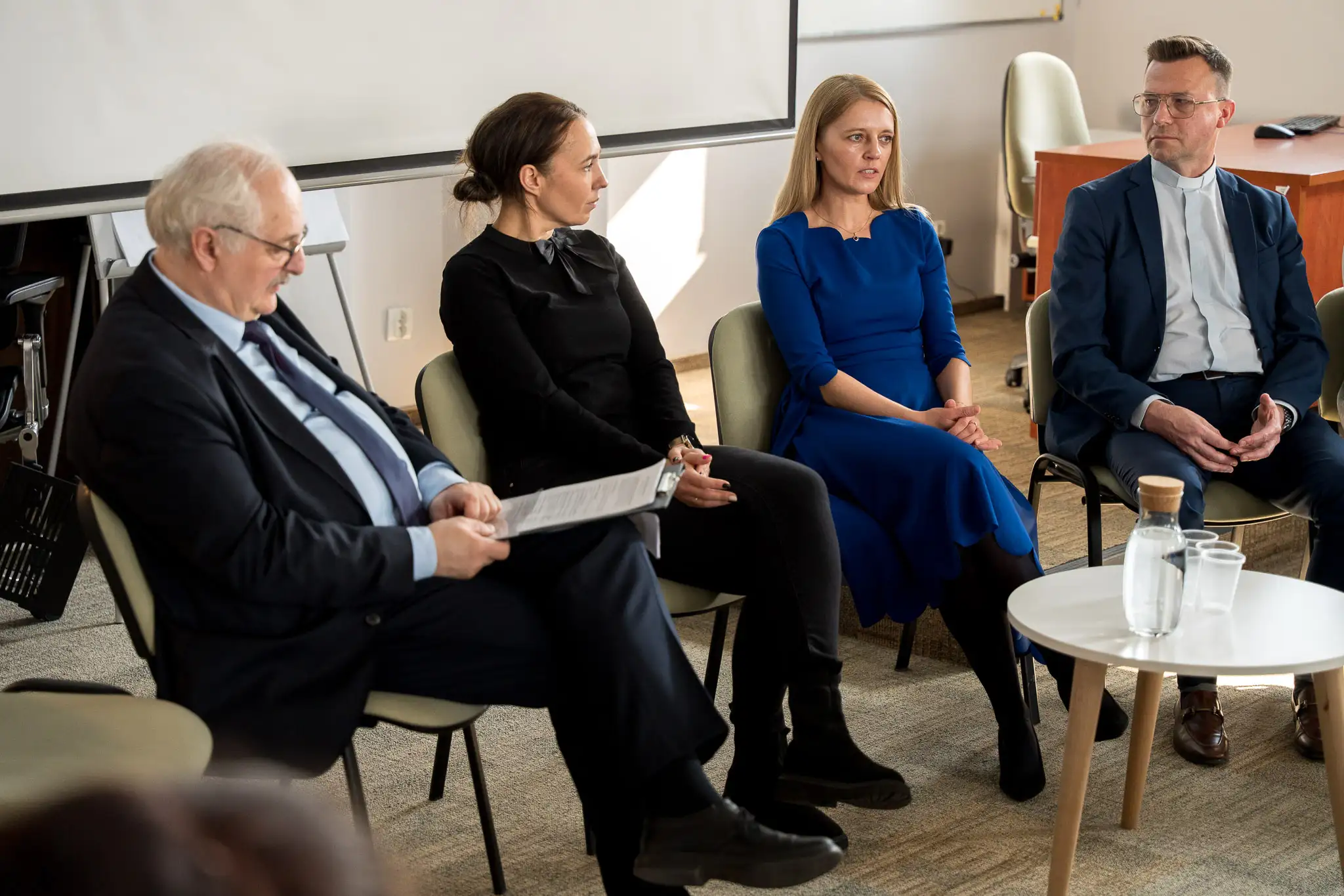 Grupa osób siedzi w półokręgu podczas spotkania lub dyskusji panelowej w sali konferencyjnej.” Jeśli chcesz, mogę przygotować także wersję rozszerzoną lub kilka wariantów do różnych zastosowań WCAG