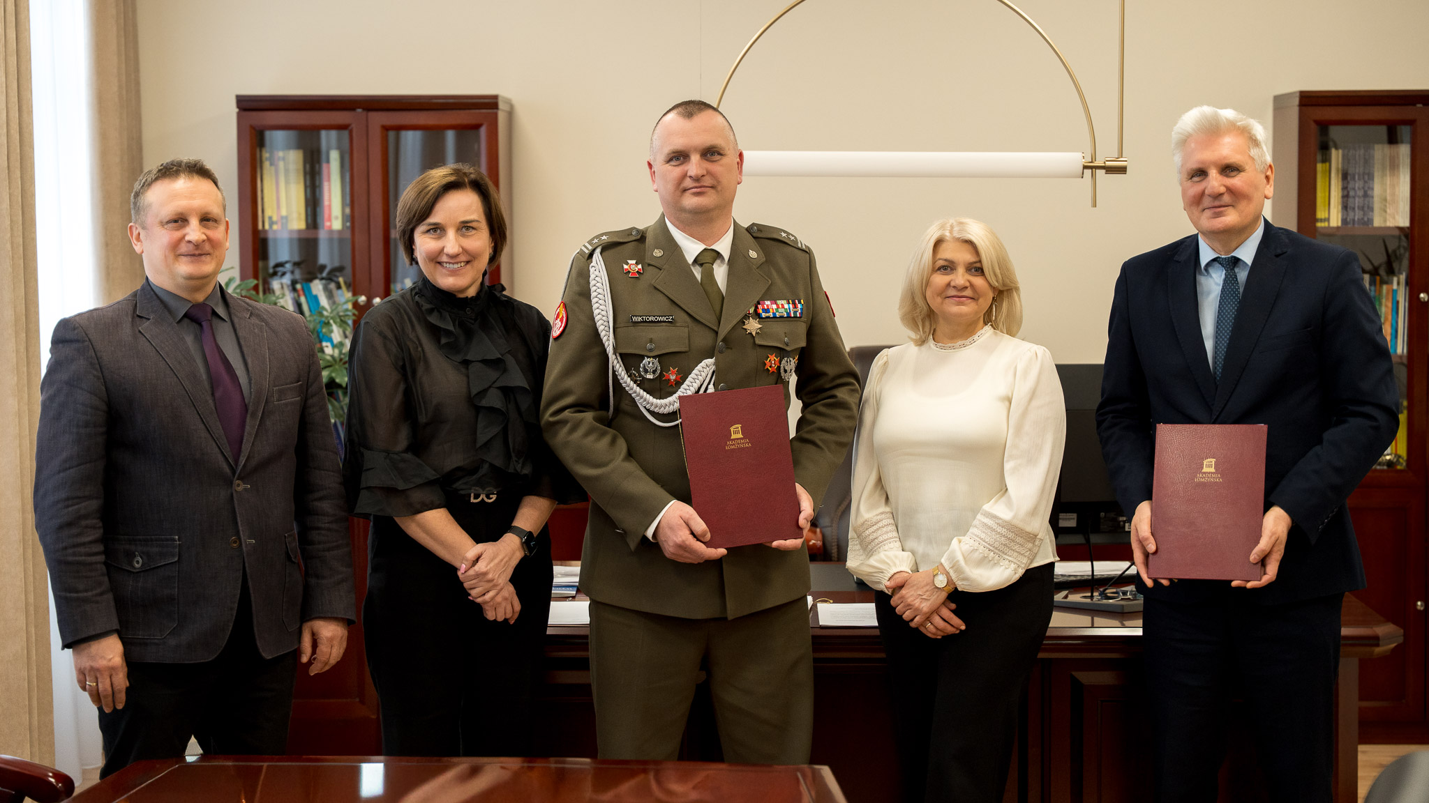 Grupa pięciu osób pozuje w biurze rektora, trzyma teczkę AŁ