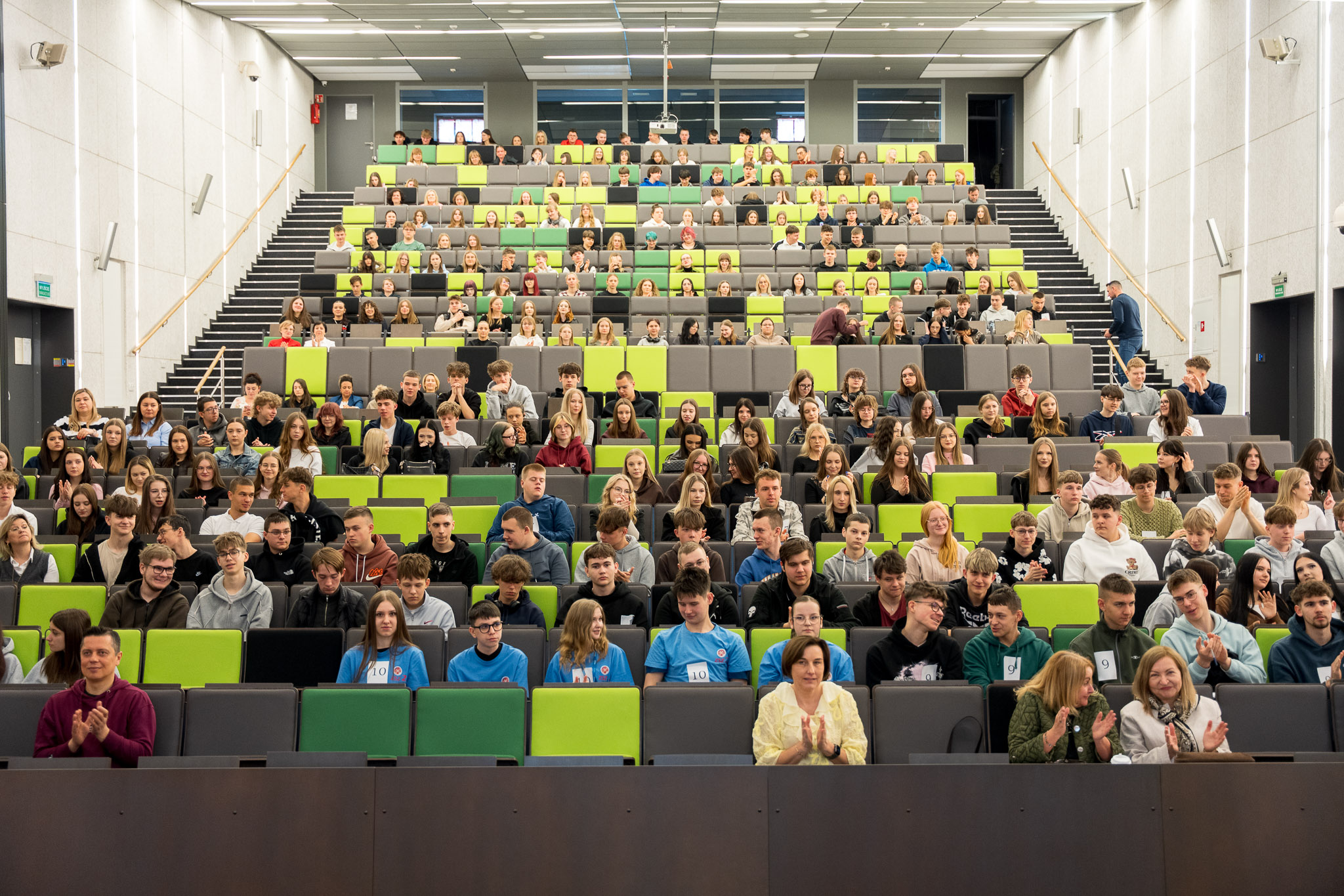 Widok auli wykładowej wypełnionej uczestnikami siedzącymi na trybunach podczas wydarzenia