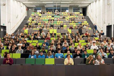 Widok auli wykładowej wypełnionej uczestnikami siedzącymi na trybunach podczas wydarzenia