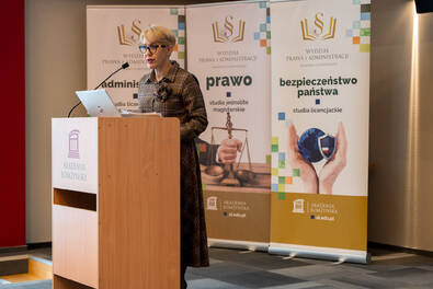 Osoba przemawia przy mównicy na tle banerów wydziału prawa i administracji.