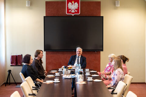 osoby przy stole prowadzą dyskusje, w tle godło Polski 