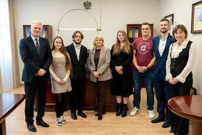 Osiem osób pozuje do wspólnego zdjęcia w biurze. W tle widać biurko, szafki z książkami i godło na ścianie.