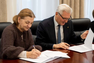 Dwie osoby stoją przy stole konferencyjnym, trzymają teczki i podają sobie ręce.