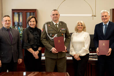 Grupa pięciu osób pozuje w biurze rektora, trzyma teczkę AŁ