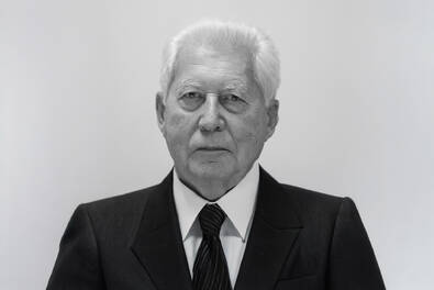 Czarno-biały portret starszego mężczyzny w garniturze i krawacie, na neutralnym tle.