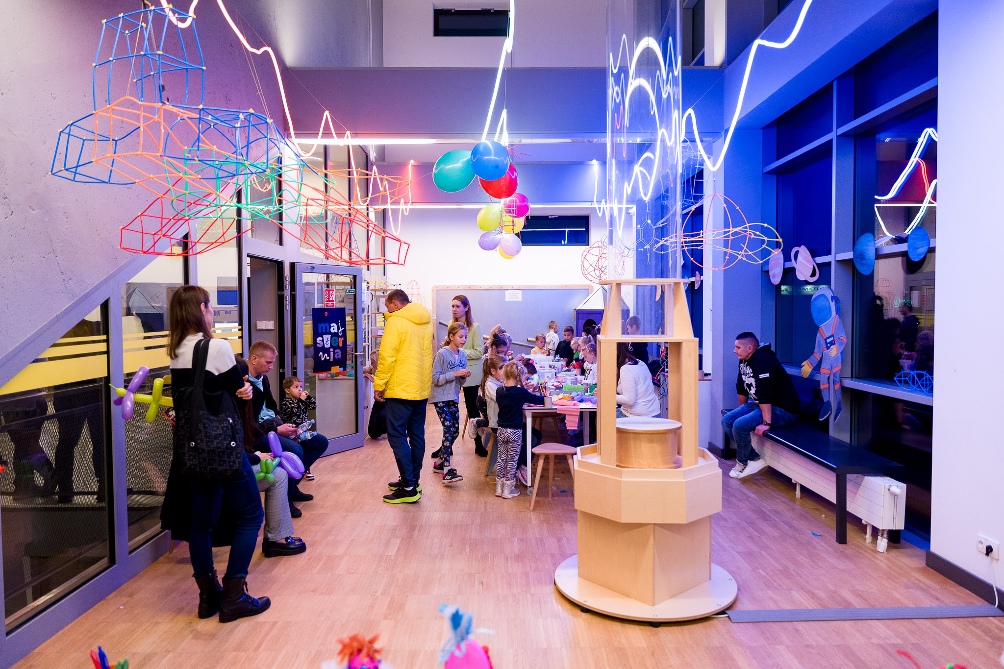 Colorful kids' activity room with bright neon lights, balloons, and children engaged in creative play.