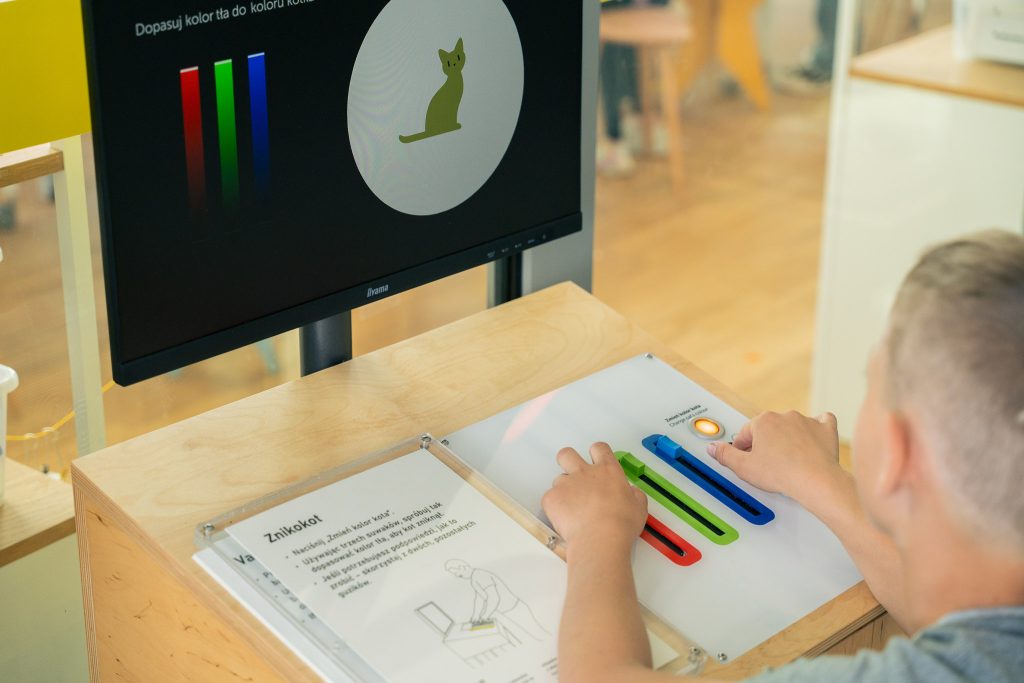 Person using color sliders to match a cat image on screen in an interactive exhibit.
