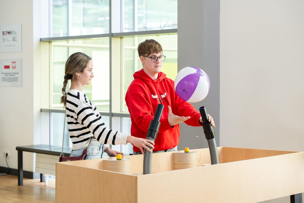 Two people experimenting with a floating beach ball in a science exhibit.