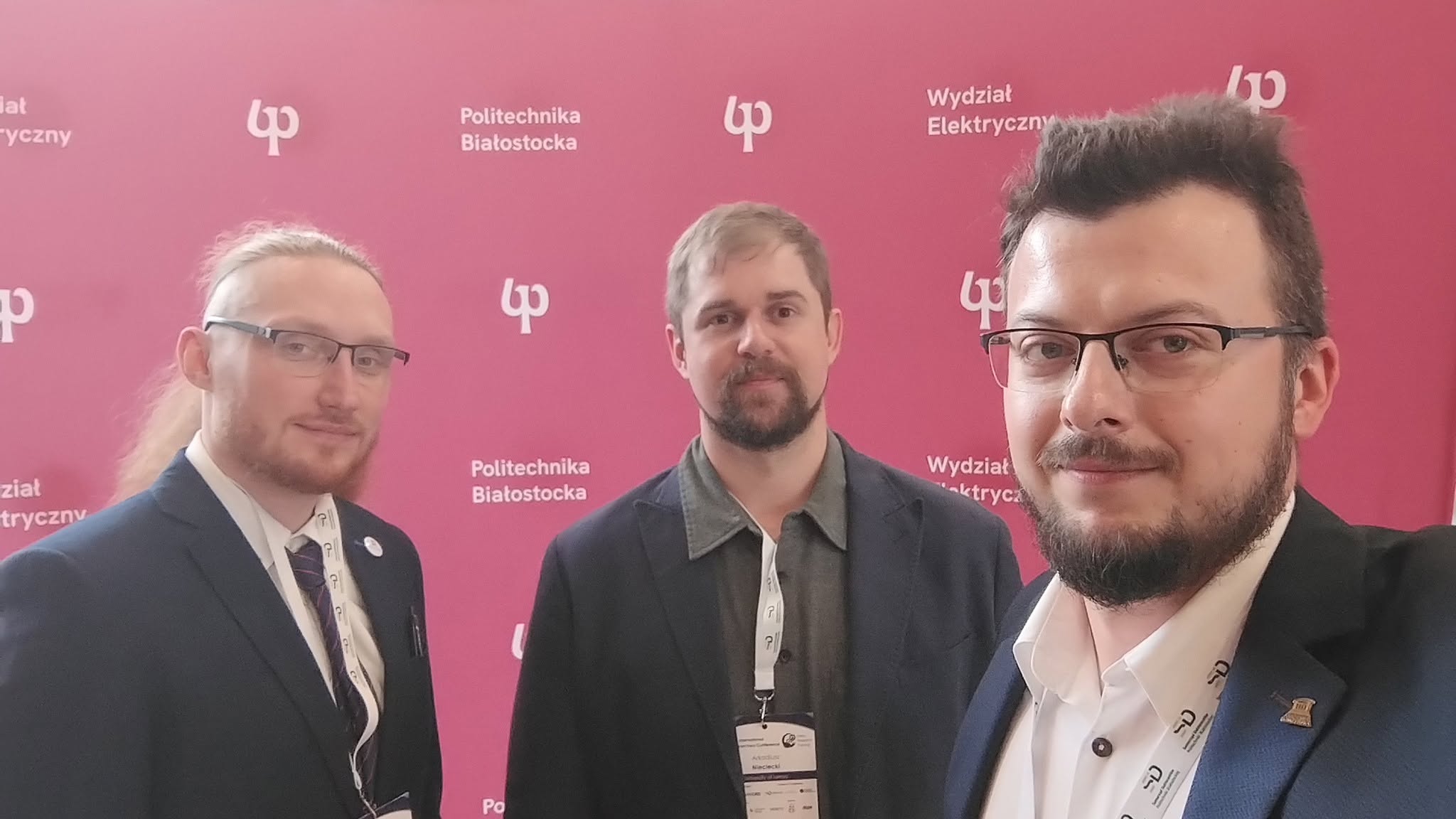 Trzech mężczyzn - pracowników Wydziału Nauk Informatyczno-Technologicznych na tle ścianki Politechniki Białostockiej