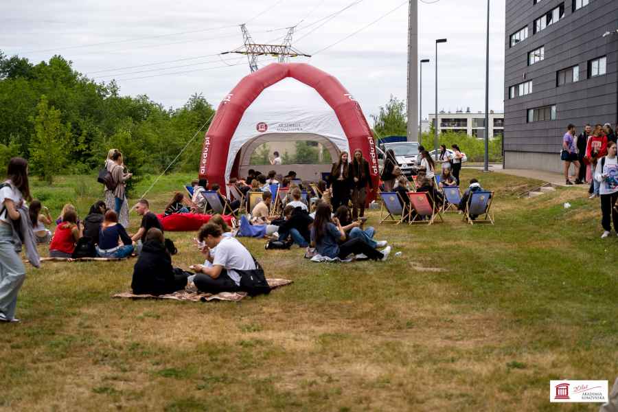 Grupa osób siedzących na leżakach i na kocykach przy namiocie