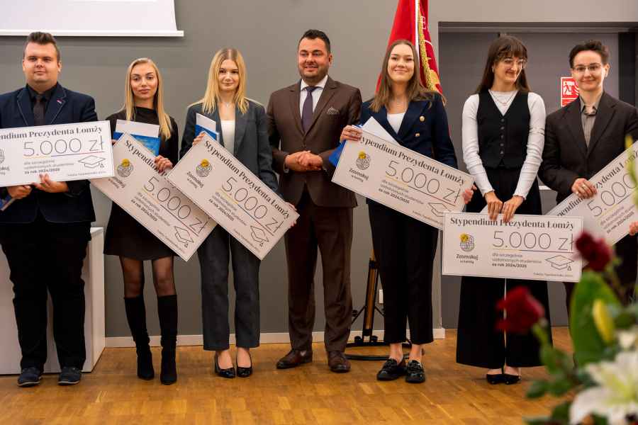Studenci trzymają karty, na których widnieje przyznana kwota stypendium Prezydenta Miasta. W środku, pomiędzy studentami stoi Prezydent Miasta Łomża- Pan Mariusz Chrznowski