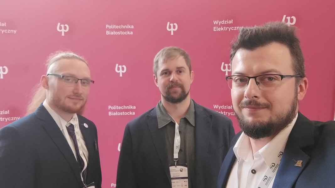 Trzech mężczyzn - pracowników Wydziału Nauk Informatyczno-Technologicznych na tle ścianki Politechniki Białostockiej
