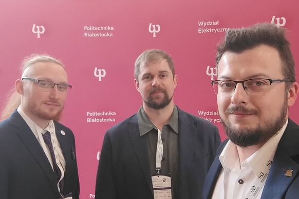 Trzech mężczyzn - pracowników Wydziału Nauk Informatyczno-Technologicznych na tle ścianki Politechniki Białostockiej