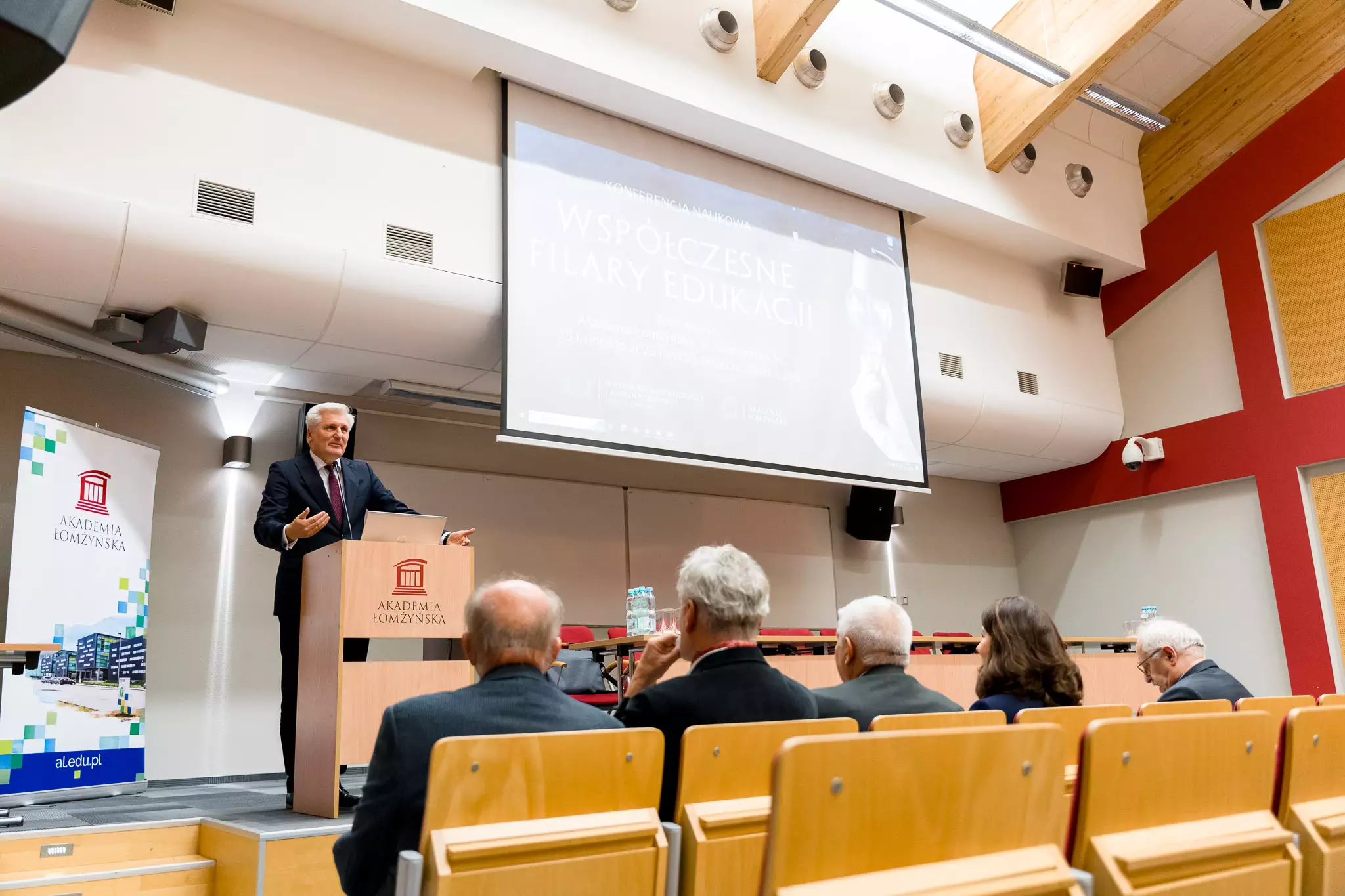 Rektor AŁ przemawia przy mównicy, w tle wyświetlana prezentacja na temat filarów edukacji