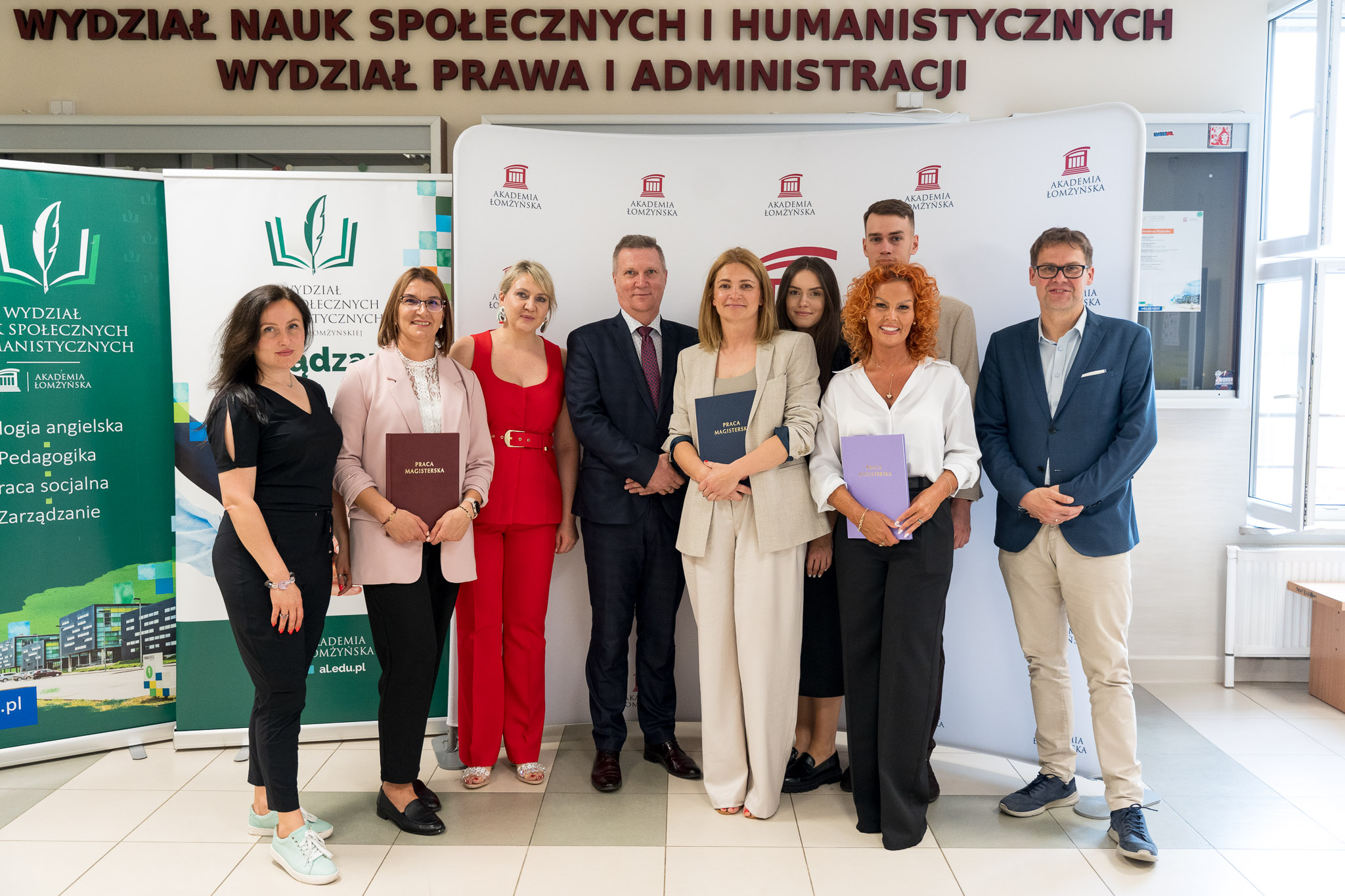 Fotografia z obron prac dyplomowych w roku 2025. Pośród absolwentów ubrana w czerwony komplet stoi dr Anna Kowalczyk-Kroenke