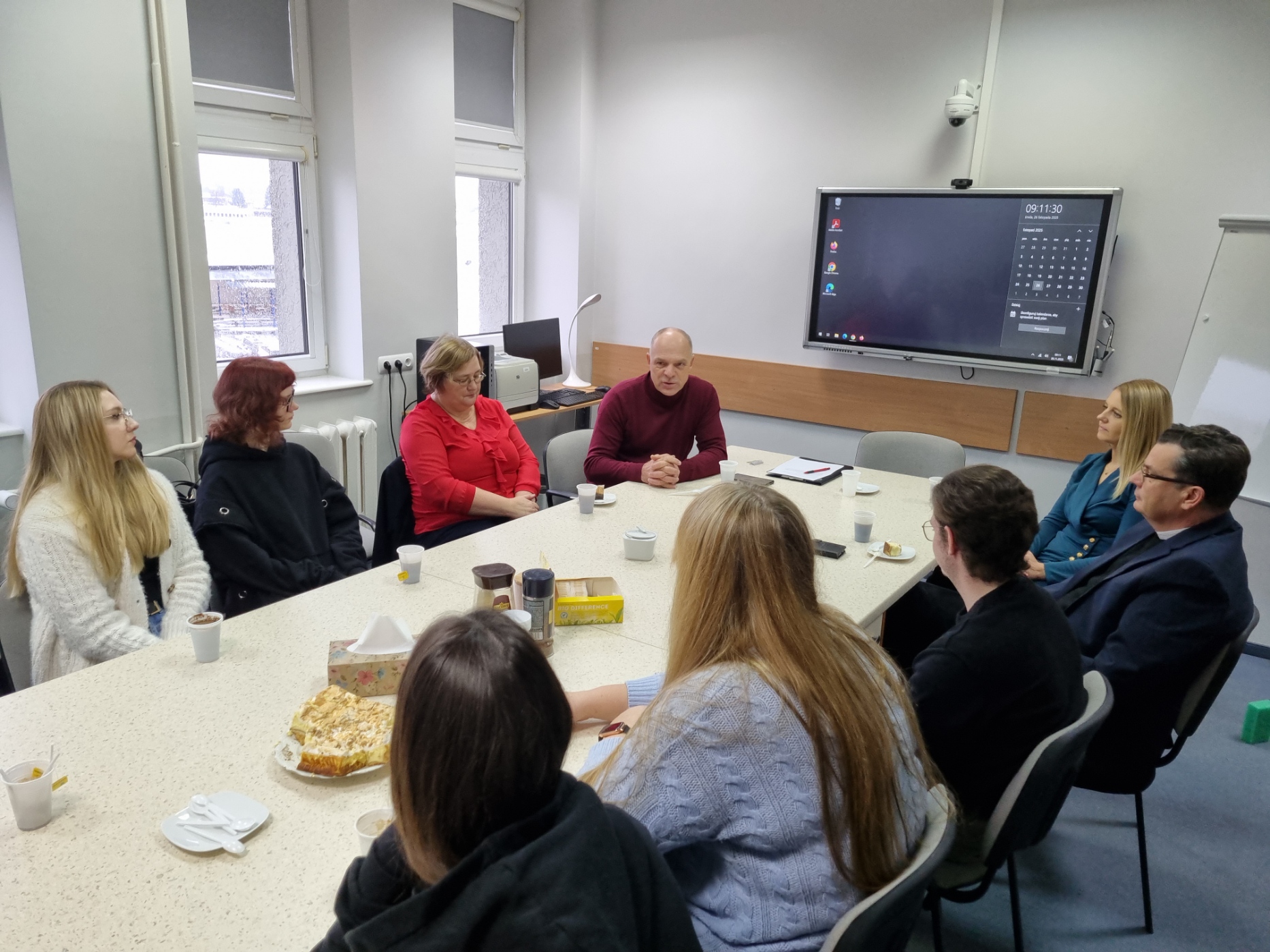 Przy długim stole siedzą studenci i pracownicy instytucji. Jedna z osób mówi