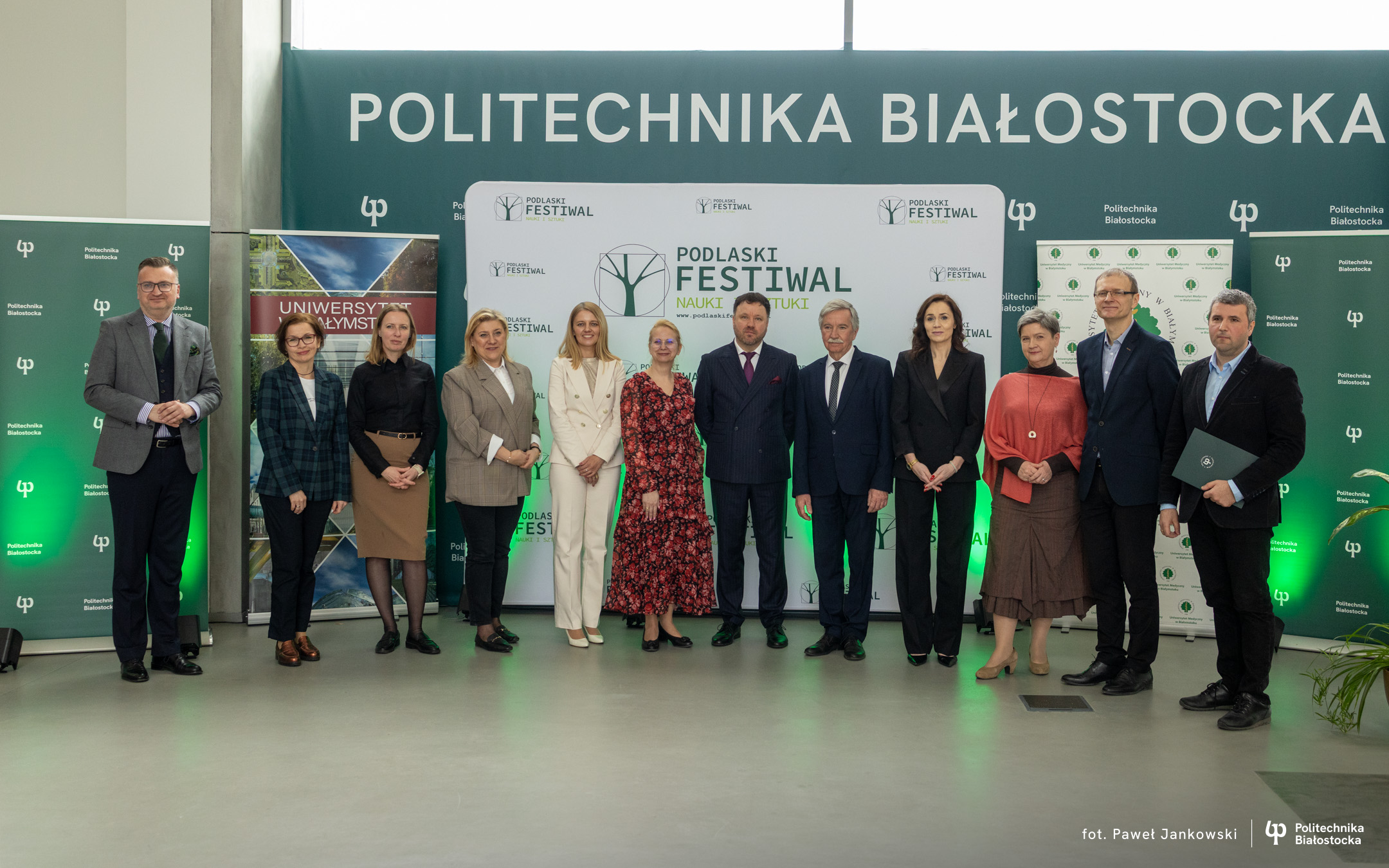 Grupowe zdjęcie uczestników wydarzenia na tle banerów Politechniki Białostockiej i Podlaskiego Festiwalu Nauki i Sztuki.