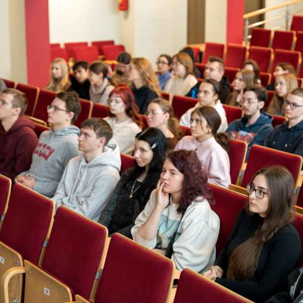 Grupa studentów siedzi w auli. Patrzą w kierunku sceny